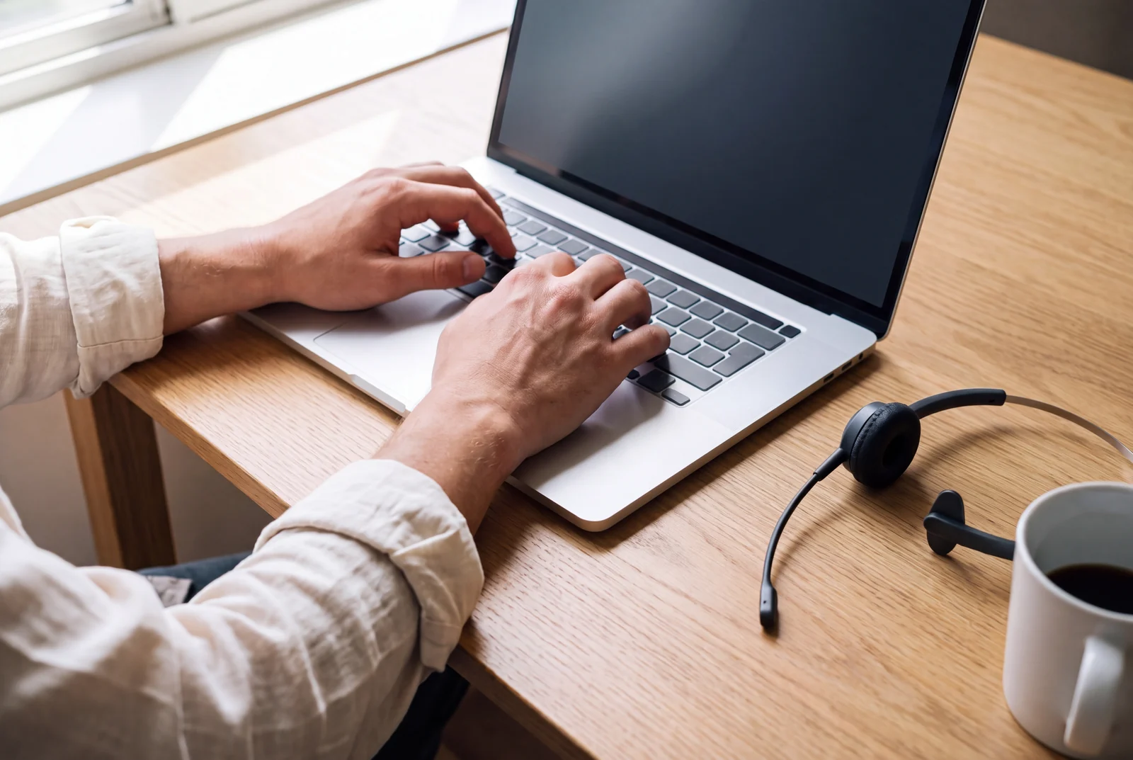 A support advisor's hands on a laptop keyboard, a headset and a cup of coffee on the desk beside it.